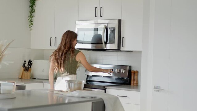 Young female turning on oven in kitchen, preheating