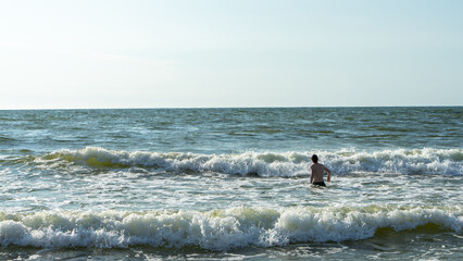 Teenager or a young man enters the waves with white foam on the Baltic Sea, Curonian Spit, Kaliningrad region, Russia. Space for text