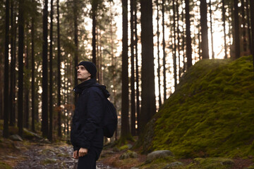 Obraz premium A caucasian man with a backpack walking in a forest on a stone path at sunset.