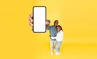 Fototapeta na wymiar Happy African Couple Showing Big Phone Blank Screen, Yellow Background