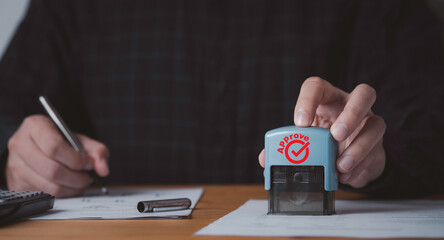 Closeup of hand holding stamping for approve document on table for business permit and ISO certificate concept.