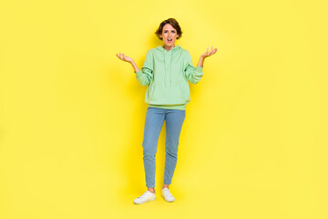 Full length photo of angry surprised lady wear green hoodie screaming rising arms isolated yellow color background