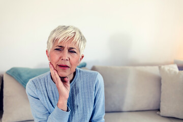 Photo of depressed ill mature woman having toothache and touching cheek. Mature woman suffering from tooth pain, caries. Gray hair female suffering from toothache, closeup.