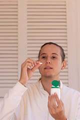Vertical view of young man about to take a pill from a white and green container for medical purpose