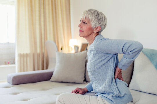 Woman feels back pain, massaging aching muscles. Mature woman feeling morning discomfort in aching back in the living room.
