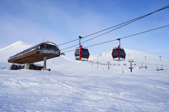 Cable car gondola at ski resort with snowy mountains on background. Modern ski lift with funitels and supporting towers high in the mountains on winter day. Ski lift station with no people.