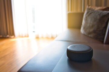 Black Amazon Alexa as Voice recognition device and white coffee mug photographed on glass table and wooden table in bed room with sunlight background