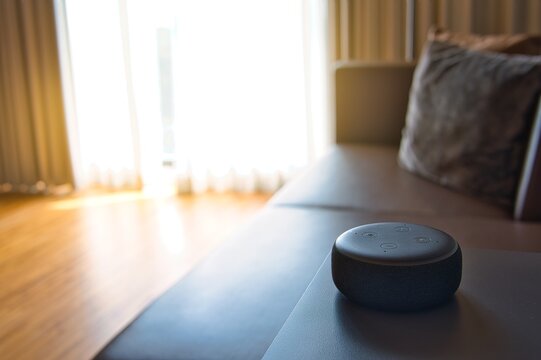 Black Amazon Alexa As Voice Recognition Device And White Coffee Mug Photographed On Glass Table And Wooden Table In Bed Room With Sunlight Background