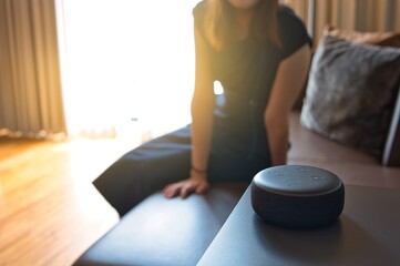 Woman sitting on a chair and talking to a speech recognition device, Amazon Alexa with sunlight...