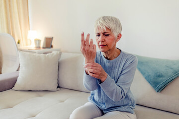 Photo of painful wrist in an elderly person. Senior woman suffering from pain in wrist at home...
