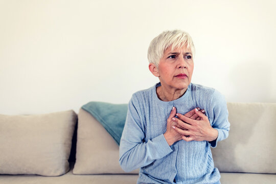 Shot of a beautiful matre woman holding her chest in discomfort due to pain at home during the day. A stressed woman who is suffering from a chest pain and touching her heart area.
