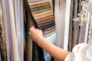 Woman choosing samples of fabric for curtain in textile store. Customer combining colors and textures indoor