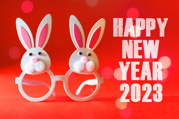 Two Toy Rabbit Bunnys symbol of new year 2023 on the red background.Inscription HAPPY NEW YEAR 2023.New Year concept.
