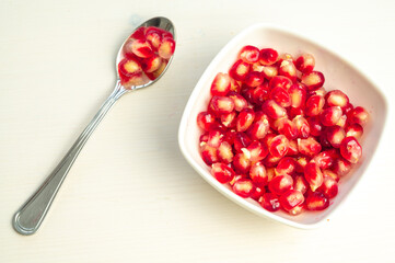 Pomegranate arils in bowl and spoon beside.
