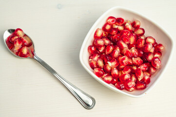 Pomegranate arils in bowl and spoon beside.
