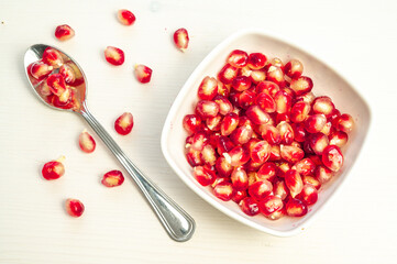 Pomegranate arils in bowl and spoon beside.
