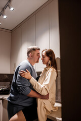 Romantic sexy young couple happily spending time hugging and kissing in cozy modern kitchen at home. Two people stand and joyfully look at each other