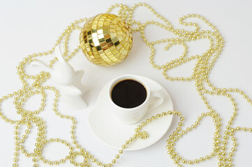 Cup of black espresso and white ceramic rabbit. Symbol of the year. Gold Christmas beads and disco ball.