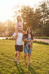 Girl is on the shoulders of man. Father and mother with daughter and little son is outdoors on the field