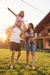 Obraz premium Girl is on the shoulders of man. Father and mother with daughter and little son is outdoors on the field