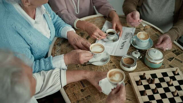 Happy senior friends sitting indoors in cafe drinking coffee or tea, laughing and having nice time together.