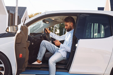 Sitting in the vehicle. Young stylish man is with electric car at daytime