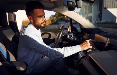 Man is sitting in the vehicle. Young stylish guy is with electric car at daytime