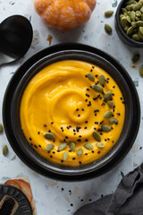 Creamy pumpkin soup in a black ceramic bowl decorated pumpkin seeds and black sesame. Terrazzo background. Close up. View from above