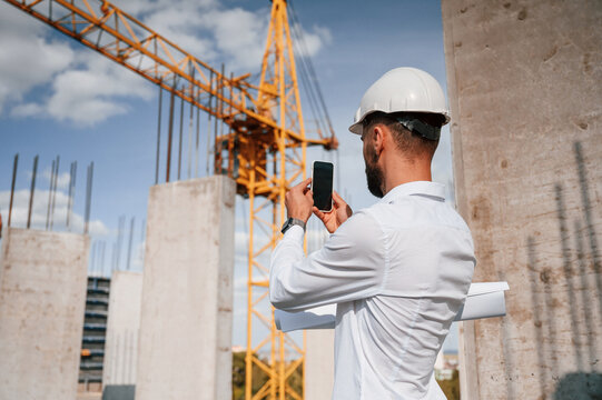 Taking a picture of place by smartphone. Man in uniform is working on the construction site