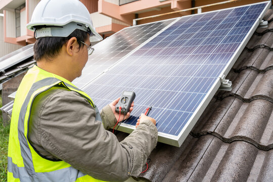 Blue Solar Photo voltaic panels system of apartment building on sunny day. Renewable ecological green energy. maintenance panels collect solar energy. Engineer holding Voltmeter.