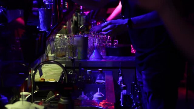 A bartender in a nightclub mixes drinks to make cocktails for guests. Night life, background.
