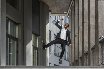 Successful businessman concept, mature african american man outside office building smiling and happy celebrating victory and triumph, boss in business suit jumping and dancing.