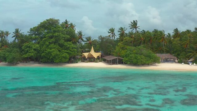 Tropical beach with azure sea, palm trees and fantastic building roof in Thinadhoo island on Vaavu atoll, Maldives.