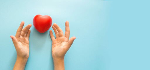 child's hands and a red heart on a blue background, copyspace on the right. Give love and care to a child, children's day. child care.adoption, baby house, orphans children concept