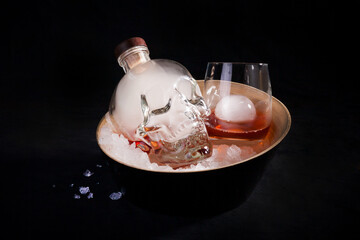 Serving an alcoholic cocktail based on rum in a skull-shaped bottle with smoke, crushed ice in a deep bowl on a black background