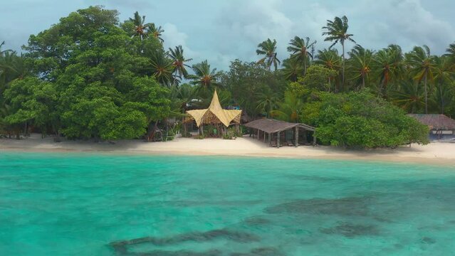 Tropical beach with azure sea, palm trees and fantastic building roof in Thinadhoo island on Vaavu atoll, Maldives.