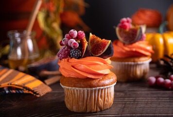 Delicious homemade autumn season spicy pumpkin cupcakes with whipped orange cream with fruit figs and frozen berries.