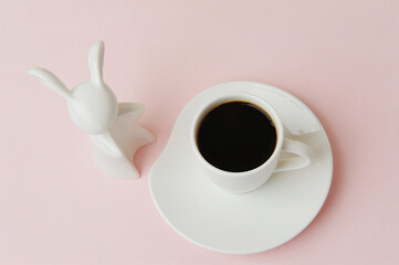 Cup of black espresso coffee and white ceramic rabbit. Symbol of the year. Soft pink background