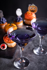 Halloween purple cocktail in glasses decorating spider. Nearby web, cupcakes and candy eyeball. Party festive celebrate concept.