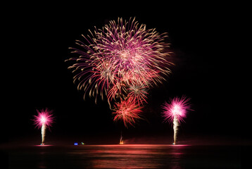 Multi coloured fireworks exploding over an ocean in the night sky.