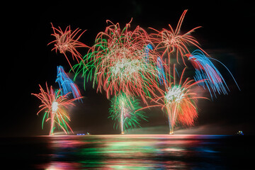 Multi coloured fireworks exploding over an ocean in the night sky.