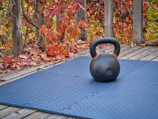 heavy iron kettlebell on an exercise mat in a backyard patio, fall scenery