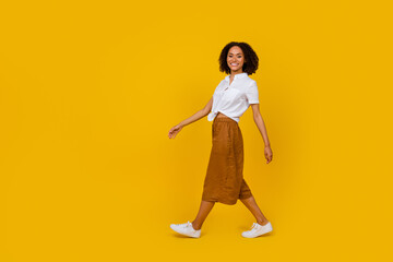 Fototapeta na wymiar Full body profile photo of gorgeous positive girl walking empty space isolated on yellow color background