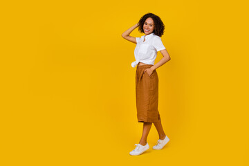 Full body portrait of pretty positive girl arm touch hair walk empty space isolated on yellow color background