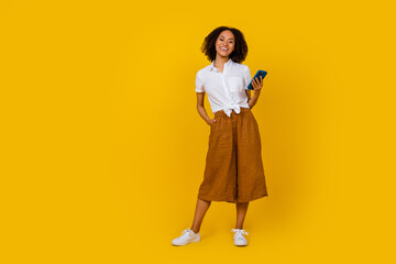 Full body portrait of pretty cheerful person hold telephone have good mood isolated on yellow color background