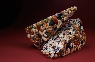 Two pieces of gozinak from various nuts with dried fruits on a red background.