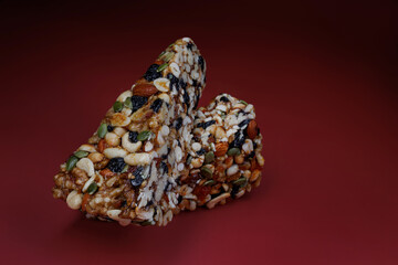 Two pieces of gozinak from various nuts with dried fruits on a red background.