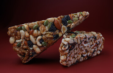 Two pieces of gozinak from various nuts with dried fruits on a red background.