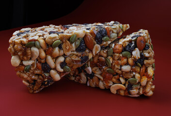 Two pieces of gozinak from various nuts with dried fruits on a red background.