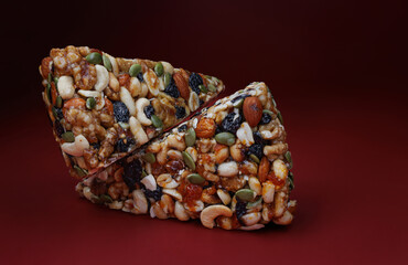 Two pieces of gozinak from various nuts with dried fruits on a red background.